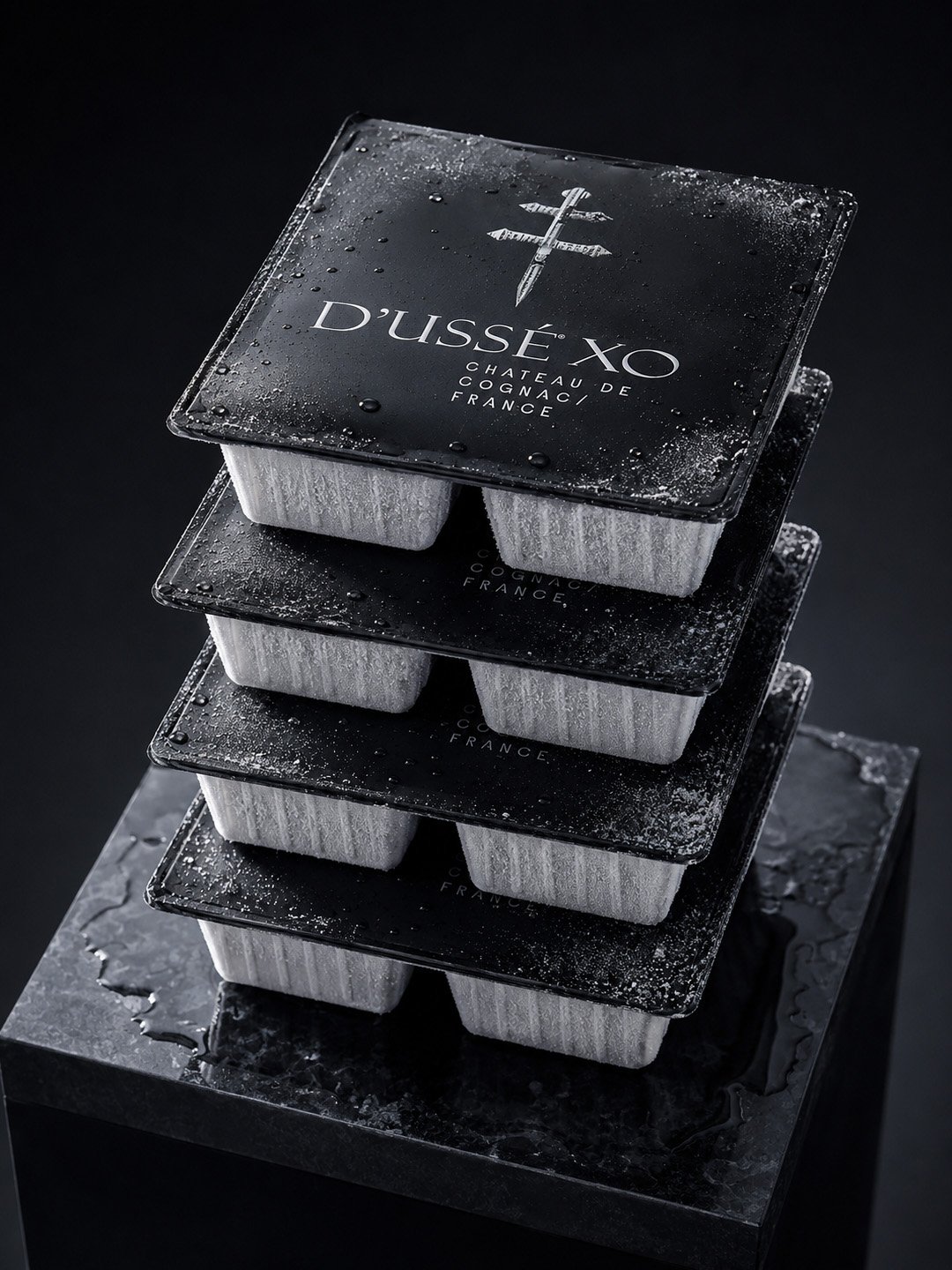 Stack of frozen D’USSÉ XO Coffee Cube packages with black branded lids and frosted white containers against a dark background.