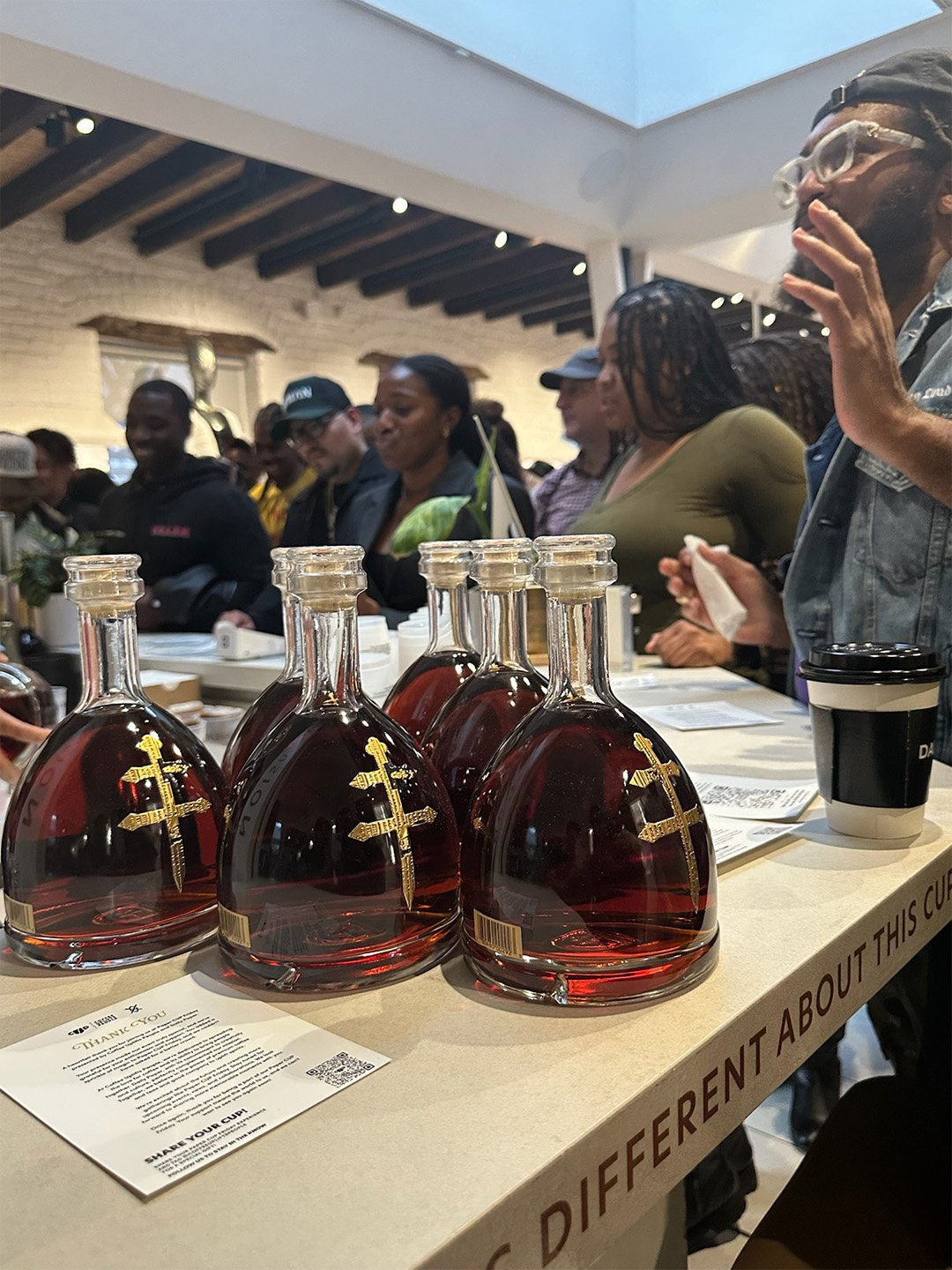 D’USSÉ bottles and guests at the Coffee Uplifts People Paper CUP Friday activation with “Something’s Different About This CUP” displayed on the counter.